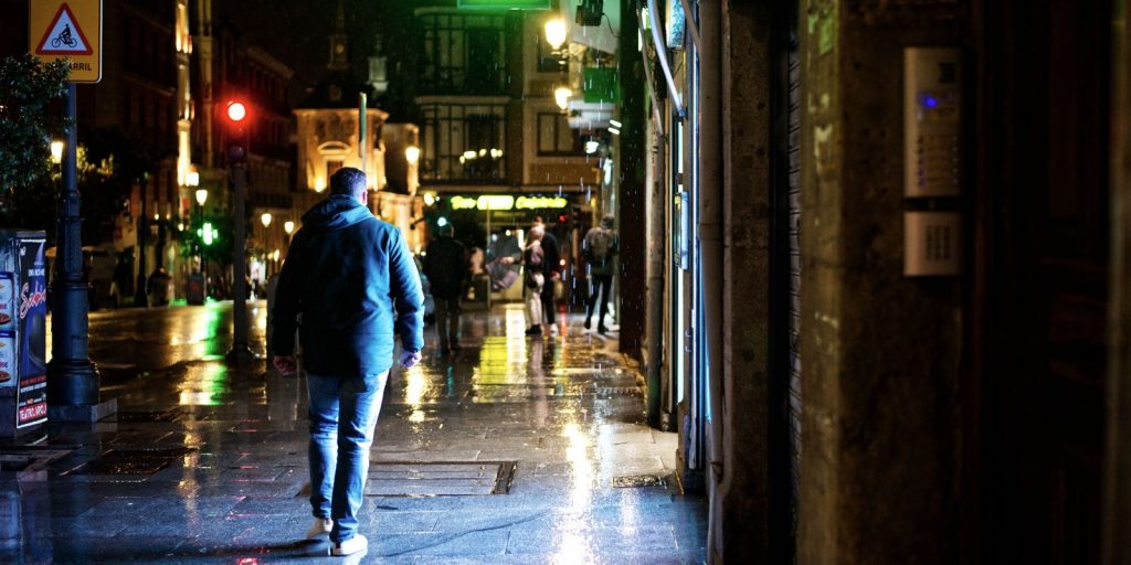 Un homme marche dans une rue mouillée éclairée au néon, sous la pluie, la nuit