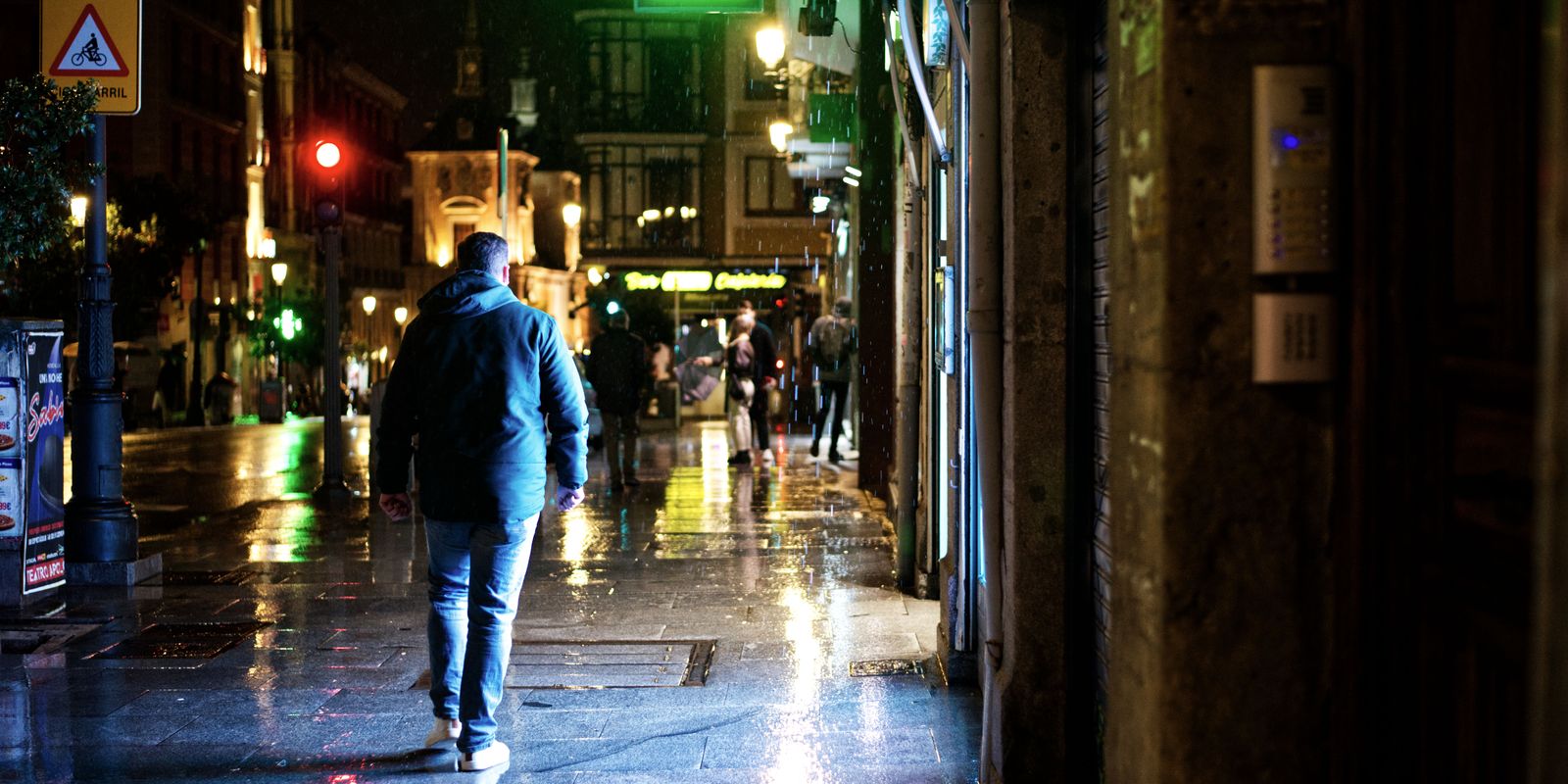 Un homme marche dans une rue mouillée éclairée au néon, sous la pluie, la nuit